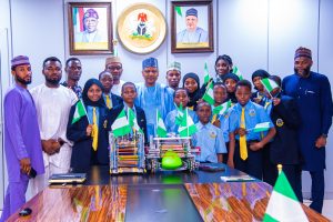 Minister of Information and National Orientation, Mohammed Idris (center), in a group photograph with the students, coaches, and the school's Executive Director, Abba Said (Extreme right).